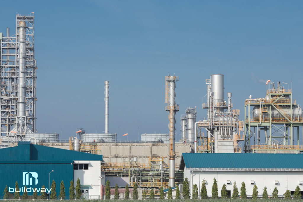 Expansive industrial manufacturing plant with metal structures, pipelines, and processing towers under a clear blue sky, designed by Buildway.