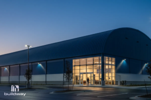 Evening view of the illuminated sports center with curved roofing and glass-fronted entryway.
