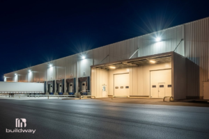 Become a Builder 3 Large steel warehouse with bright exterior lighting at night, built by Buildway. A modern example of professional construction and quality workmanship.