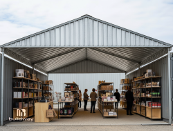Spacious steel-framed commercial shed used as a retail or storage space, featuring organized shelving and people browsing products. Built by Buildway for versatile business and warehouse applications.