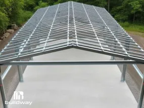 Steel framing structure for a Quonset prefab foundation system by Buildway, installed over a concrete base with open surroundings and trees in the background.